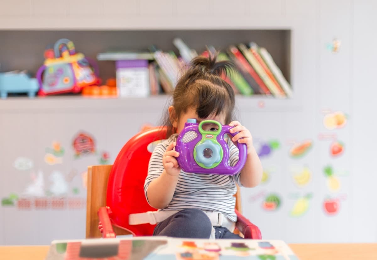 A child looking through a toy camera in a bright playroom